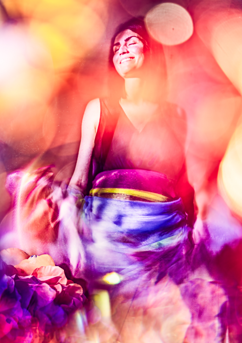 A woman smiling with her eyes closed, surrounded by vibrant, colorful lights and abstract patterns, creating a dreamlike and joyful atmosphere.