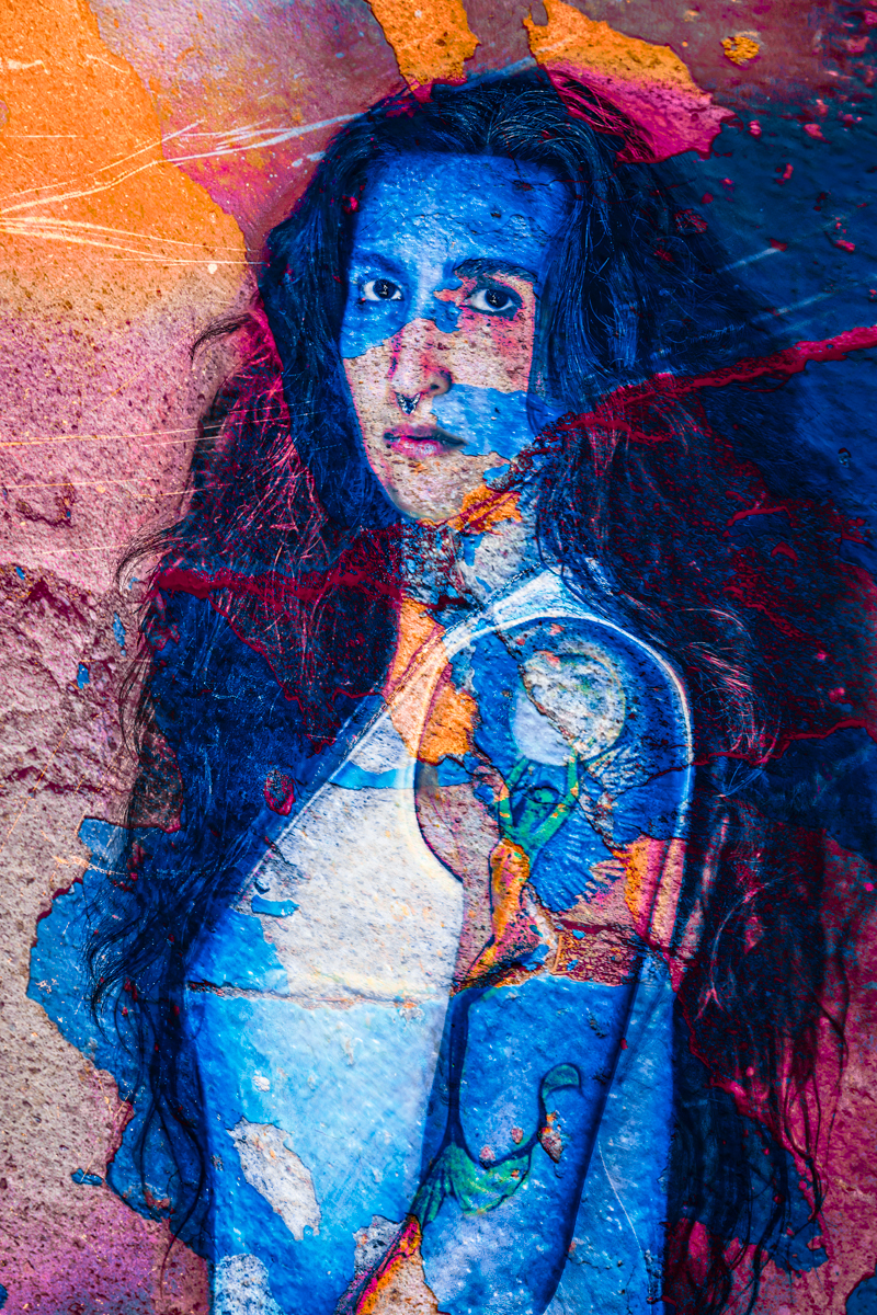 A surreal double exposure of a woman with long hair and a tattoo, blended with vivid layers of textured, colorful street art and paint splatters in blue, orange, and magenta.