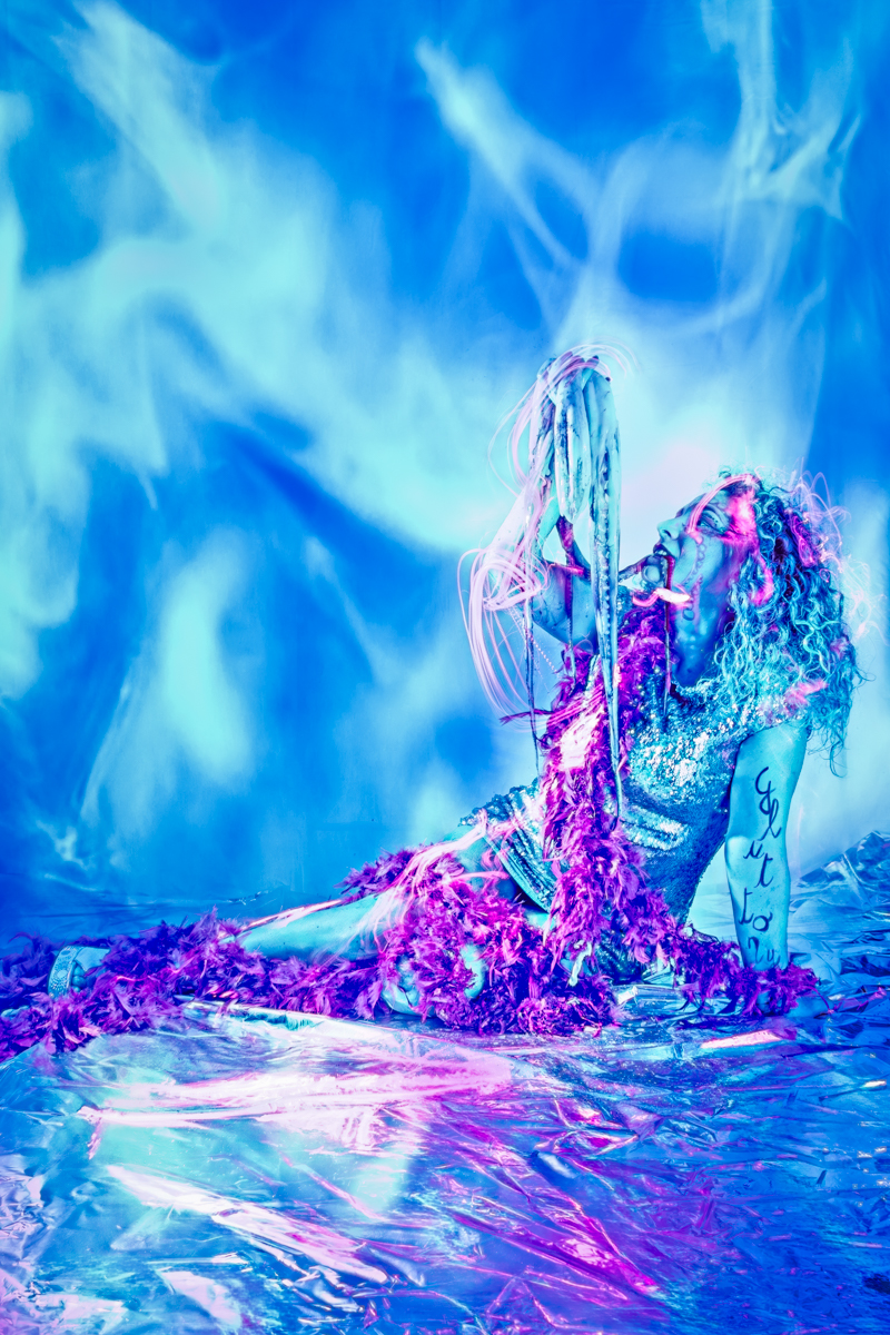 A woman’s face, partially obscured by a dark purple and blue smoke cloud, lies amidst an octopus, simulating a scene from The Little Mermaid, suggesting the underwater kingdom.