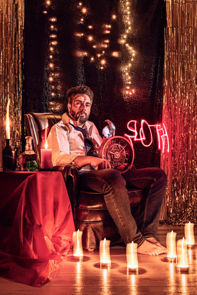 A man, depicting Captain Hook, sits languidly in a plush red armchair, surrounded by candles and a half-finished bottle of rum, representing the sin of sloth.